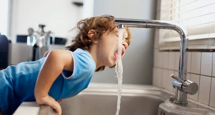 jeune enfant buvant de l'eau au robinet